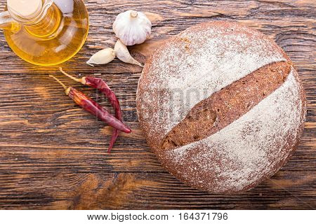 whole fresh loaf of round rye bread with a crispy crust standing beside olive oil garlic and chilli