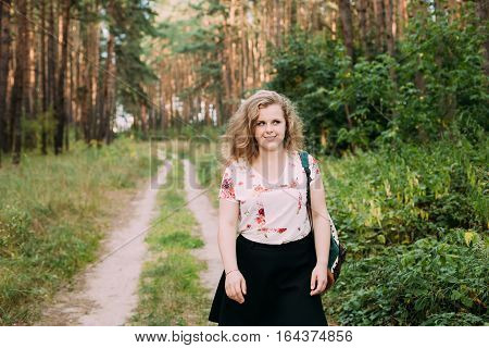 Young Pretty Plus Size Caucasian Happy Smiling Girl Woman In White T-Shirt And Black Short Skirt Walking Full-Length On Road In Summer Pine Forest