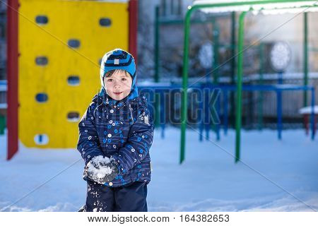 Funny little kid boy in colorful clothes playing outdoors during snowfall. Active leisure with children in winter on cold snowy days. Happy child having fun and playing with snow