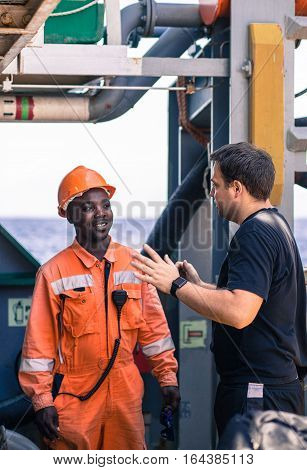 friendship of nations on board of ship/vessel. European Chief officer instructing African seaman on deck before job.