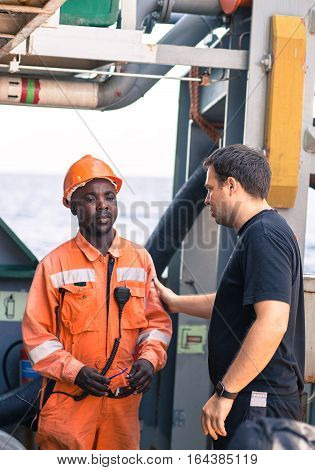friendship of nations on board of ship/vessel. European Chief officer instructing African seaman on deck before job.