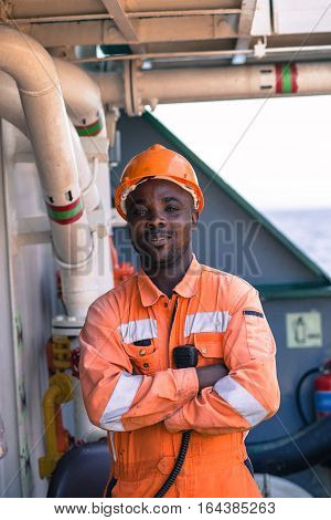 young african seaman standing on deck dressed in coverall and safety helmet with VHF radui station waiting for work orders