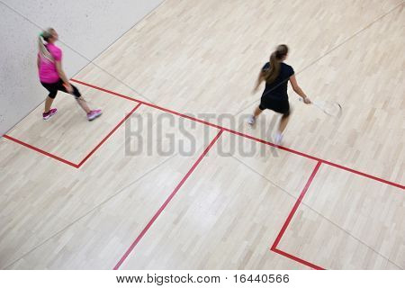 Due giocatori di squash femminile in azione veloce su un campo da squash (immagine sfocata movimento; immagine a colori dai toni)