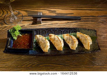Yaki gedza with sauce in a ceramic pot on a wooden table