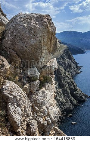 Russia Crimea. Rocks which snap into the sea near Balaklava. Hot Crimean sun-scorched grass rare green bushes mozhevelnik. Huge boulders miraculously hold on a slope.