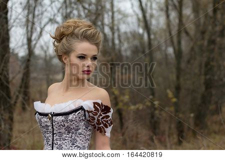 Beautiful young lady in gorgeous vintage white dress in the forest professional makeup and hairstyle. Late autumn cold. Portrait outdoors.