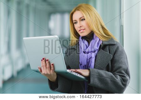 Portrait of blond businesswoman working on laptop in lobby.