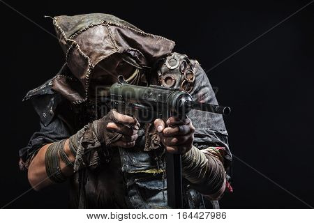 Nuclear post apocalypse life after doomsday concept. Grimy survivor with homemade weapons aiming a gun. Studio closeup portrait on black background