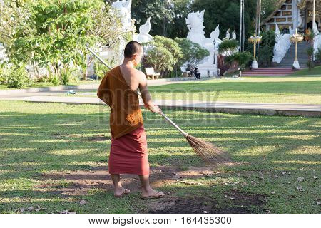 Buddhist Monk Working With Broom Sweeps Lawn From Fallen Leaves In Temple