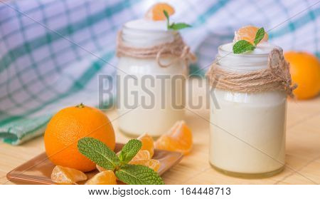 Fresh organig natural white yogurt in glass jars with tangerine and green mint