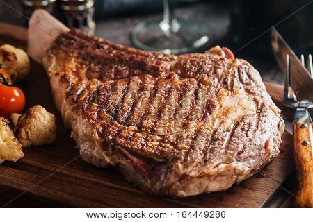 Succulent grilled tomahawk beef steak on the bone with red wine, seasonings, fresh rosemary and grilled vegetables on cutting board
