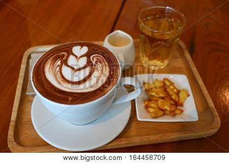 Nice latte art on the cup of hot chocolate with syrup and biscuits