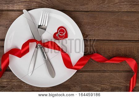 Valentines day table setting with plate, fork, knife, red heart, ringa nd ribbon. Valentines day background. Still life