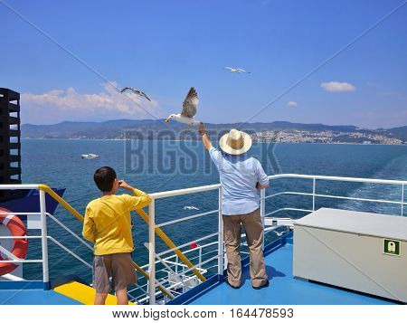 Man feeding seagulls in flight on ferry deck.