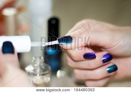 hands of a young woman who is painting her nails a transparent top coat over dark green metalized nail varnish
