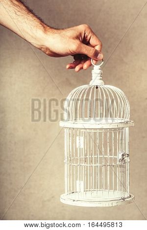 Hand holding an empty cage. Absence of ideas and dreams. Freedom and hope. Hand holding an empty cage. Absence of ideas and dreams. Freedom and hope. Solitude and loneliness concept. The arm of a man holding a white cage with nothing inside. Freedom of ex