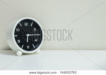 Closeup black and white alarm clock for decorate show a quarter past six or 6:15 a.m.on white wood desk and cream wallpaper textured background with copy space