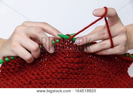 Girl's hands are knitting a red muffler out of wool with green knitting needles.