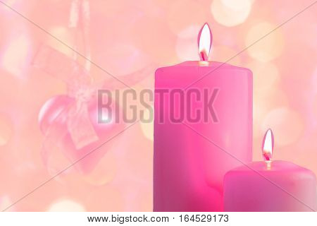 Pink burning candles on a blurred festive background close-up