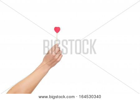 Woman's hand holding red heart shape on stick. White brick wall baskground. Valentine concept