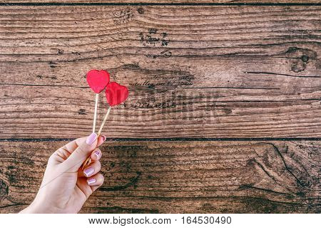 Woman's hand holding two red hearts shape on stick. Dark wooden baskground. Valentine concept