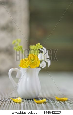 Ranunculus bouquet in miniature diminutive jug. Macro close-up photo with soft focus bouquet of buttercup flowers. Rustic colored wooden background