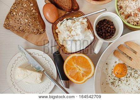 Fried Eggs in the Frying Pan, Breakfast Ingredients Orange, Bread, Butter, Beans Coffe. Kitchen Accessories. Cooking Morning Food. White Table. Top View