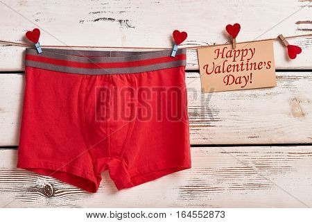 Boxer briefs on wooden surface. Greeting card, heart, clothespin. Valentine's Day surprise for boyfriend.