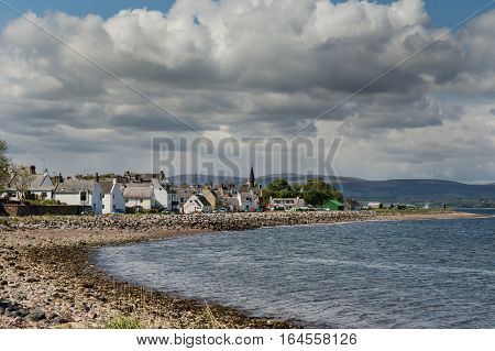 Cromarty Scotland - June 3 2012: The historic fishing and trading village on the North Sea bay under heavy loaded cloudy sky. Shot from distance. Hills in background. Rocky shore.