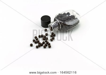 Black pills of traditional medicine or Black bolus near bottle stack on white background.
