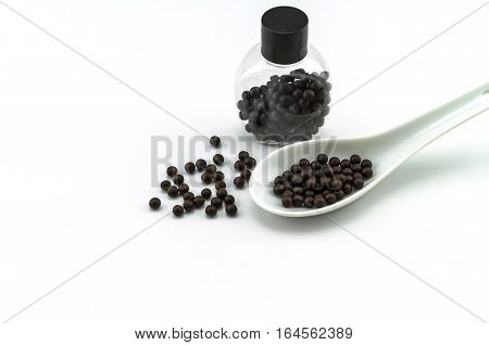 Black pills of traditional medicine or Black bolus near bottle and white ceramic spoon on white background.