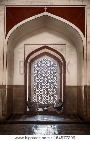DELHI, INDIA - NOVEMBER 20, 2016: Two men frame a window inside Humayan's Tomb in Delhi, India which is richly decorated with inlaid stone. The building is a UNESCO World Heritage site.