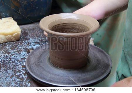 A clay pot on a pottery wheel, pottery craft, moulding the pot with your hands, sculpting hands