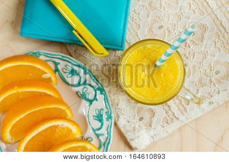 Plate with slices of oranges and orange juice. Phonebook with pencil and fresh orange juice. Focus on the glass.
