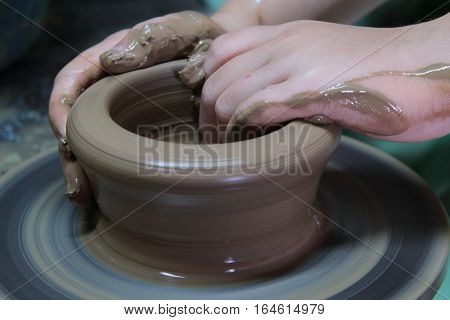 hands of a potter, creating an earthen jar on a pottery wheel