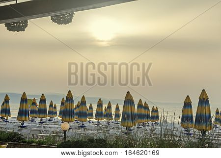 The Black Sea Shore At Sunrise, Beach Sand With Umbrellas And Sunbeds, Clouds And Blue Water.
