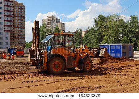 Yellow tractor works on construction site at summer sunny day