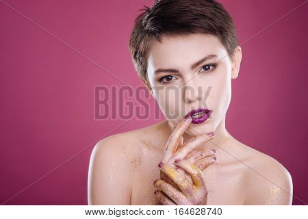 fFashion show. Attractive professional young model touching her lips and looking at you while posing on pink background