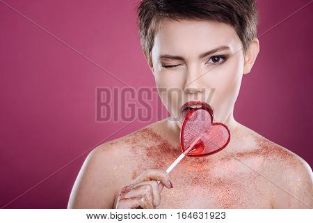 Involved in process. Joyful content young woman looling at you while licking lollipop