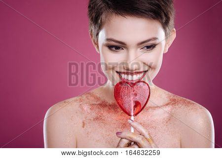 Brighten your ife. Cheerful beautiful woman holding lollipop and smiling while posing against pink background