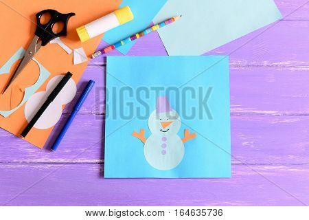 Creating a children winter paper card. Tutorial. Paper snowman card, scissors, markers, pencil, glue stick, colored paper set, snowman templates on wooden table. Children paper art on winter vacation