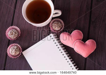 chocolate balls, mini marshmallows, pink felted hearts and notebook on purple wooden background Romantic love background Valentines day background top view place for text