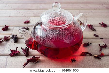 Hibiscus tea in glass teapot and dry flower on wooden background