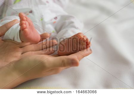 baby feet on mothers hands on white blanket