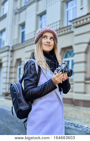 Beautiful girl photographer photographing the old town with retro camera. She is wearing a knitted cap