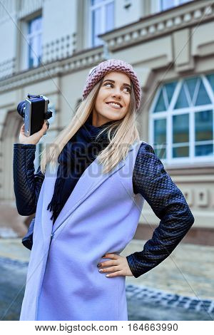 Beautiful girl photographer photographing the old town with retro camera. She is wearing a knitted cap