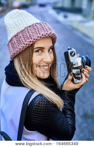 Beautiful girl photographer photographing the old town with retro camera. She is wearing a knitted cap
