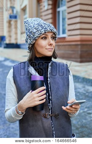 The girl with a smartphone and Thermocup, is walking through the old town