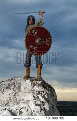 Knight on a rock with a sword against blue cloudy sky