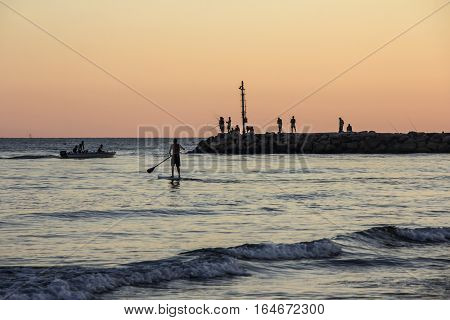 Sunset on Tyrrhenian sea, view of breakwater, SUP surfer, harbor and seacoast of Terracina, Lazio, Italy